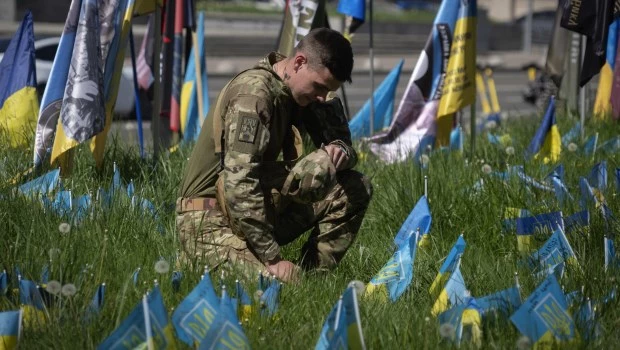 Un soldado arrodillado en la plaza de la Independencia en Kiev, Ucrania, el miércoles 1 de mayo de 2024, rodeado de pequeñas banderas nacionales que simbolizan a los soldados ucranianos muertos en la guerra con Rusia.