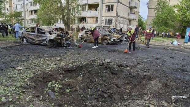 Trabajadores municipales limpian cerca de autos quemados y un cráter hecho por un dron en una zona residencial luego del ataque aéreo ruso en Kiev, Ucrania (4 de mayo de 2025)