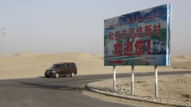 Un auto en un desierto donde un cartel dice "Bienvenido al Nuevo Pueblo Unidad Hotan", en Hotan, en la región occidental china de Xinjiang. AP