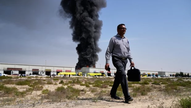 Un hombre se aleja tras observar una columna de humo negro que se eleva desde un almacén en la zona industrial de Sharjah, Emiratos Árabes Unidos.