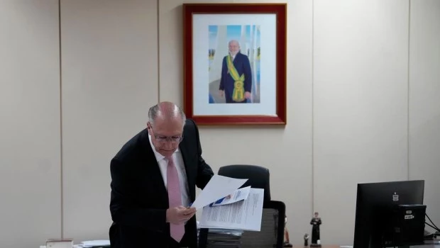 El vicepresidente de Brasil, Geraldo Alckmin, toma algunos papeles de un escritorio frente a una foto de Luiz Inácio Lula da Silva.